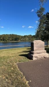 Scenic view of Washington Crossing State Park featuring a historic monument by the Delaware River, surrounded by trees under a clear blue sky.