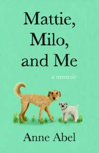 The book cover says Mattie, Mile, and Me in large letters in the top center. Below the words is an illustration of two dogs, one a larger dog with textured light brown fur and the other a smaller dog with white fur and a cropped tail. 